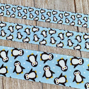 May include: Three ribbons with a light blue background and a repeating pattern of cartoon penguins. The penguins are black and white with yellow feet and beaks. The ribbons vary in width and are arranged vertically.