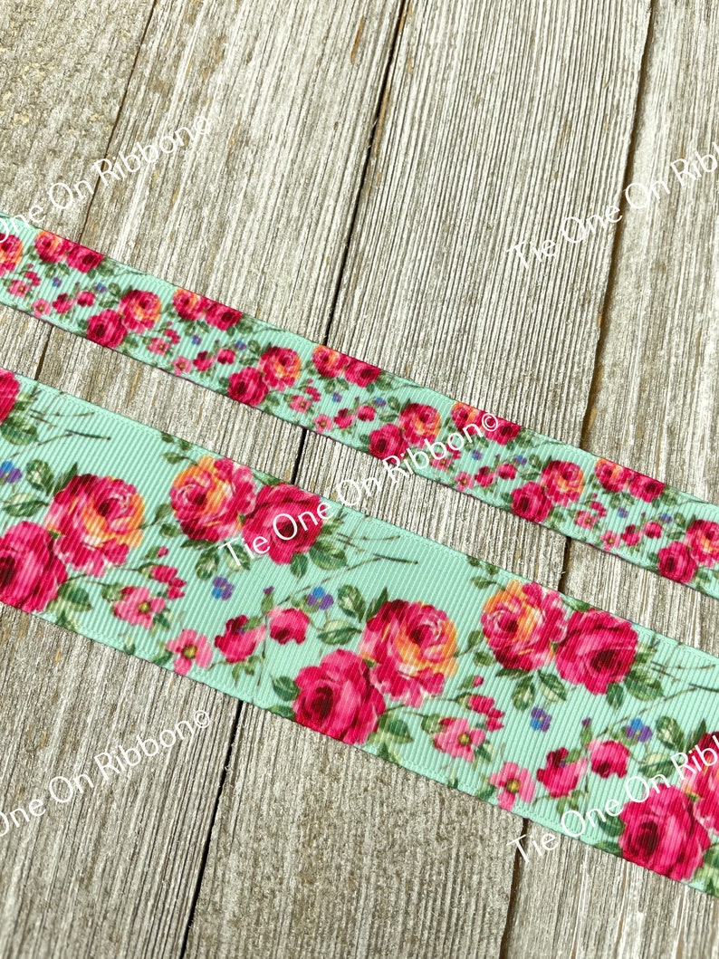 Puede incluir: Primer plano de una cinta azul claro con estampado floral con rosas rosas y naranjas. La cinta est&aacute; sobre una superficie de madera.