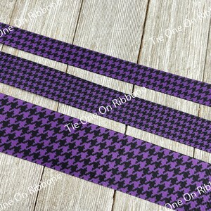 May include: Three strips of purple and black houndstooth ribbon. The ribbon is on a wooden surface.
