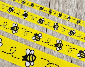 May include: Yellow ribbon featuring a repeating pattern of black and white bees and dotted flight paths. The ribbon is shown in various widths, highlighting the bee design.