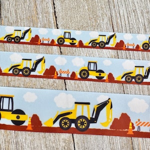 May include: Light blue ribbon featuring a repeating pattern of yellow construction vehicles, brown hills, orange traffic cones, and white clouds. The ribbon is suitable for crafting and embellishments.