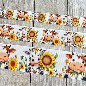 May include: White ribbon featuring a repeating pattern of cartoon cows with sunflowers. The cows have brown and white markings, and the sunflowers are yellow with brown centers. The ribbon is suitable for crafts and decorations.
