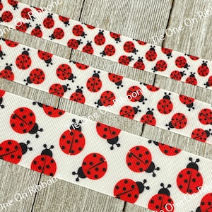 Puede incluir: Cinta blanca con un patrón repetido de mariquitas rojas con puntos negros. La cinta está sobre una superficie de madera.