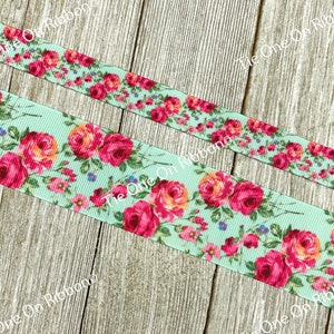 Puede incluir: Primer plano de una cinta azul claro con estampado floral con rosas rosas y naranjas. La cinta est&aacute; sobre una superficie de madera.