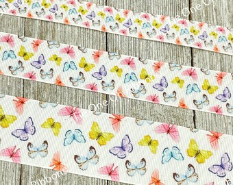 May include: White ribbon with a repeating pattern of colourful butterflies. The butterflies are in shades of pink, yellow, blue, and purple. The ribbon is on a wooden surface.