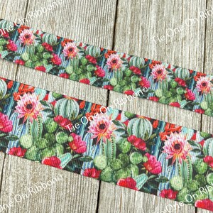 May include: A close-up of a colorful ribbon with a repeating pattern of cacti and flowers. The ribbon is on a wooden surface.