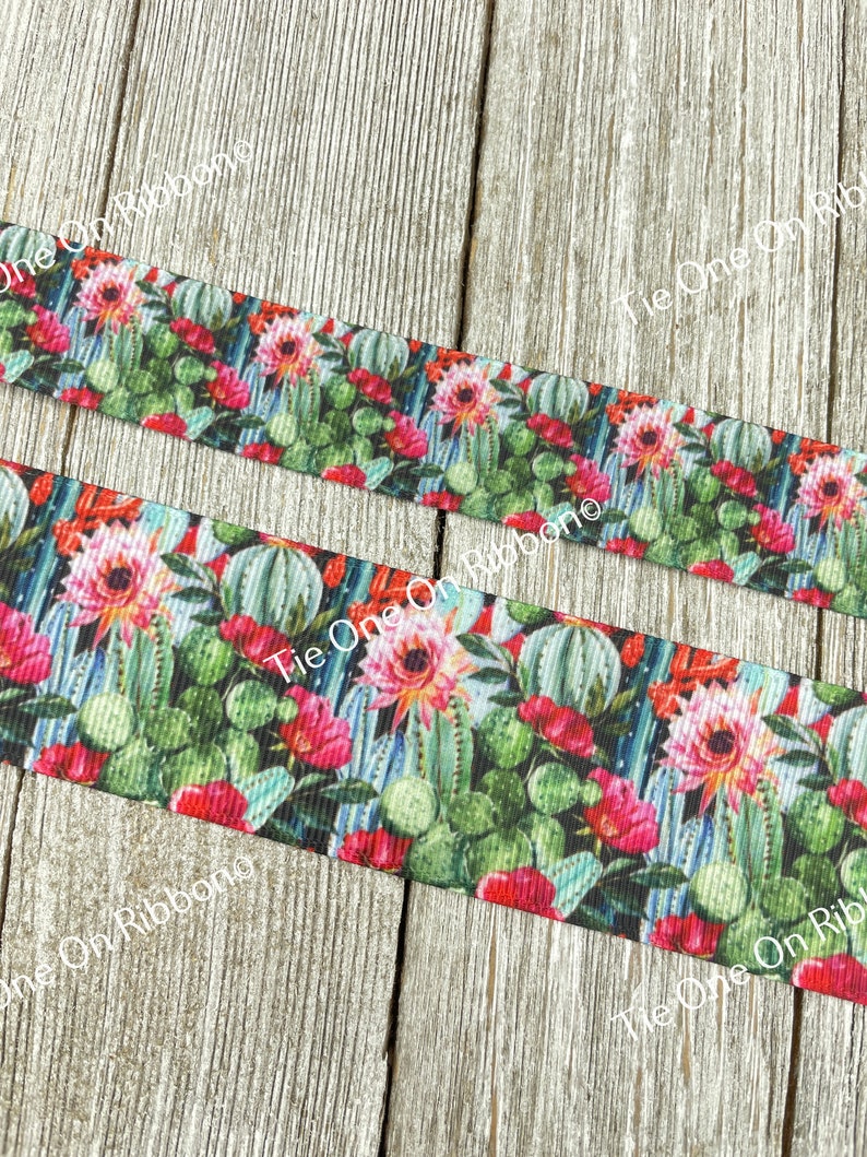 May include: A close-up of a colorful ribbon with a repeating pattern of cacti and flowers. The ribbon is on a wooden surface.