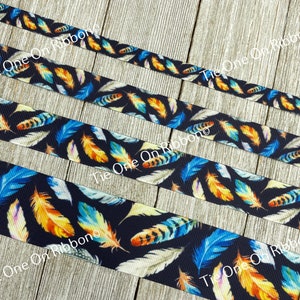 May include: Close-up of several ribbons with a repeating feather pattern. The feathers are in shades of blue, orange, and white against a dark navy background. The ribbons are arranged diagonally across a wooden surface.