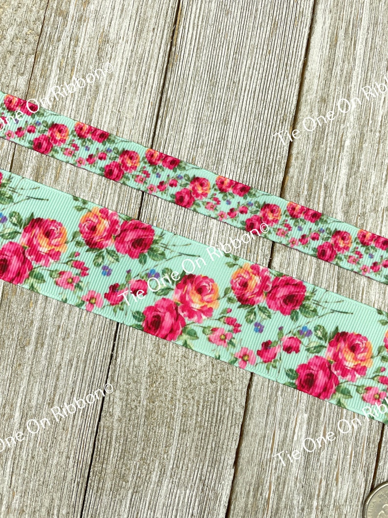 Puede incluir: Primer plano de una cinta azul claro con estampado floral con rosas rosas y naranjas. La cinta est&aacute; sobre una superficie de madera.