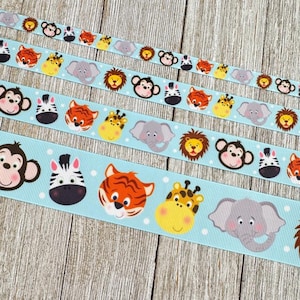 May include: Four ribbons with a light blue background and white polka dots. Each ribbon features a repeating pattern of cartoon animal faces, including monkeys, zebras, tigers, giraffes, elephants, and lions. The ribbons are arranged on a wooden surface.