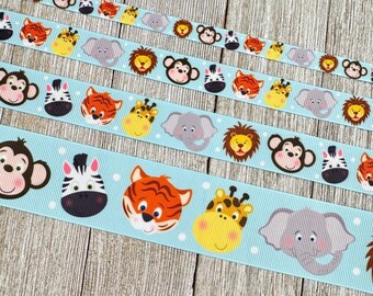 Può includere: Quattro nastri con sfondo azzurro chiaro e pois bianchi. Ogni nastro presenta un motivo ripetuto di facce di animali dei cartoni animati, tra cui scimmie, zebre, tigri, giraffe, elefanti e leoni. I nastri sono disposti su una superficie di legno.
