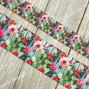 May include: A close-up of a green, pink, and blue ribbon with a cactus and flower print. The ribbon is on a wooden surface.