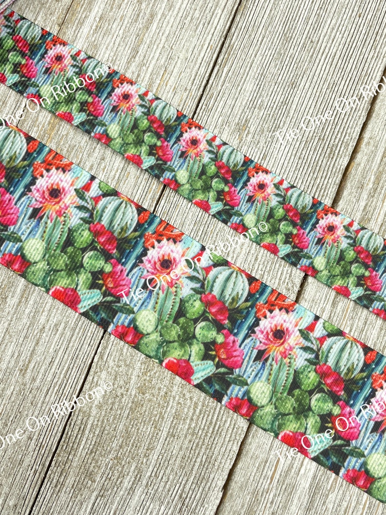 May include: A close-up of a green, pink, and blue ribbon with a cactus and flower print. The ribbon is on a wooden surface.