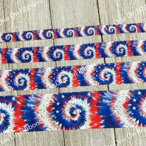 May include: Red, white, and blue tie dye ribbon with white stars. The ribbon is on a wooden surface.
