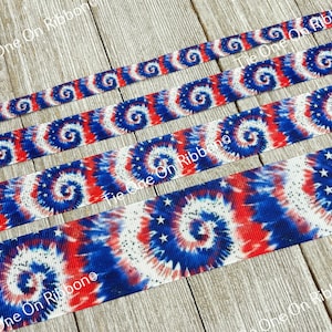 May include: Red, white, and blue tie-dye ribbon with white stars. The ribbon is on a wood background.