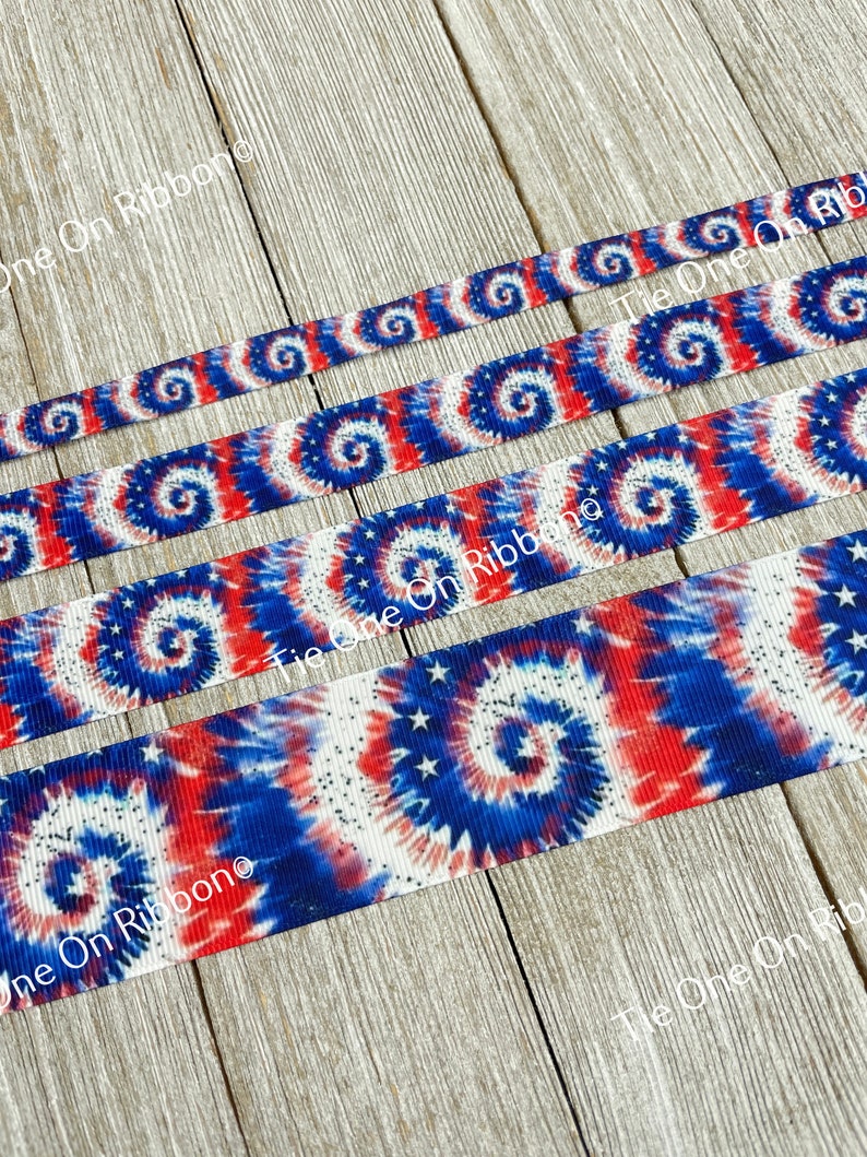 May include: Red, white, and blue tie-dye ribbon with white stars. The ribbon is on a wood background.