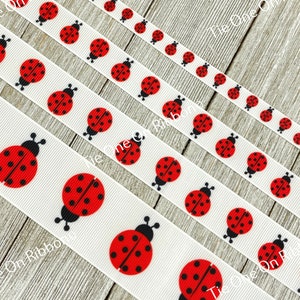 Può includere: Cinque nastri di raso bianco con un motivo ripetuto di coccinelle rosse con punti neri. I nastri sono disposti a scalare, con il nastro superiore che è il più corto e il nastro inferiore che è il più lungo.