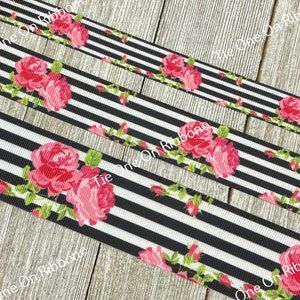 May include: Black and white striped ribbon with pink roses printed on it. The ribbon is on a wooden surface.