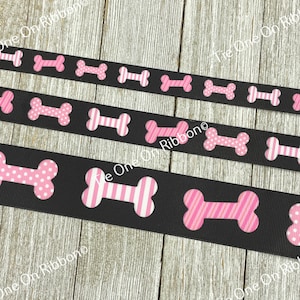 May include: Black ribbon with pink bone-shaped designs. The bones have different patterns, including polka dots, stripes, and a solid pink color.