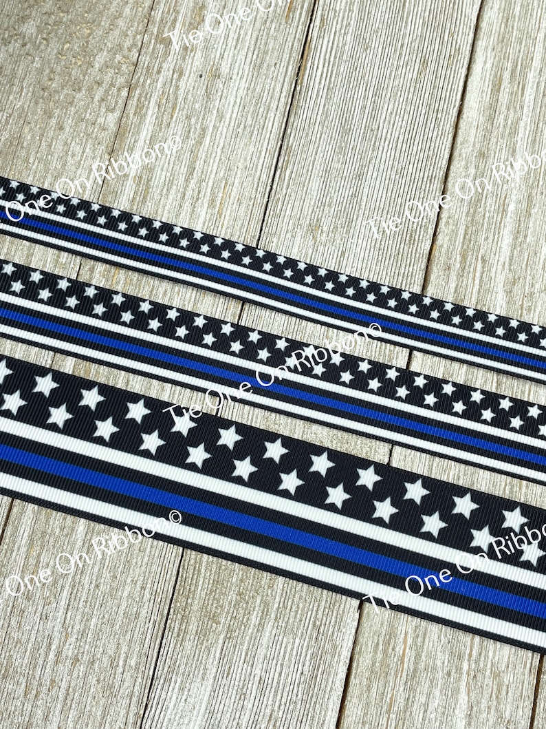 May include: Black and white ribbon with a thin blue line and white stars. The ribbon is on a wooden surface.