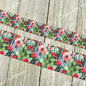 May include: A close-up of a colorful ribbon with a cactus and flower print. The ribbon is green, pink, red, and white. The ribbon is on a wooden surface.