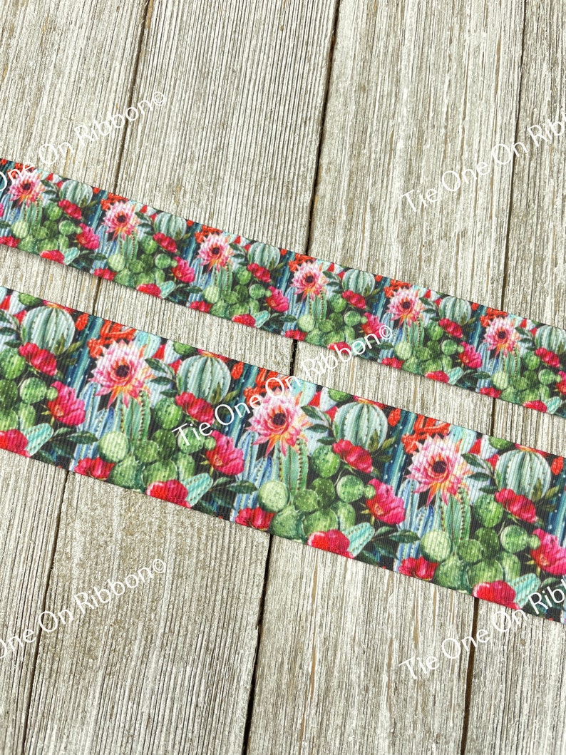 May include: A close-up of a colorful ribbon with a cactus and flower print. The ribbon is green, pink, red, and white. The ribbon is on a wooden surface.