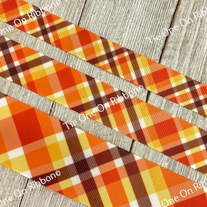 May include: Orange, brown, yellow, and white plaid ribbon. The ribbon is on a wood background.