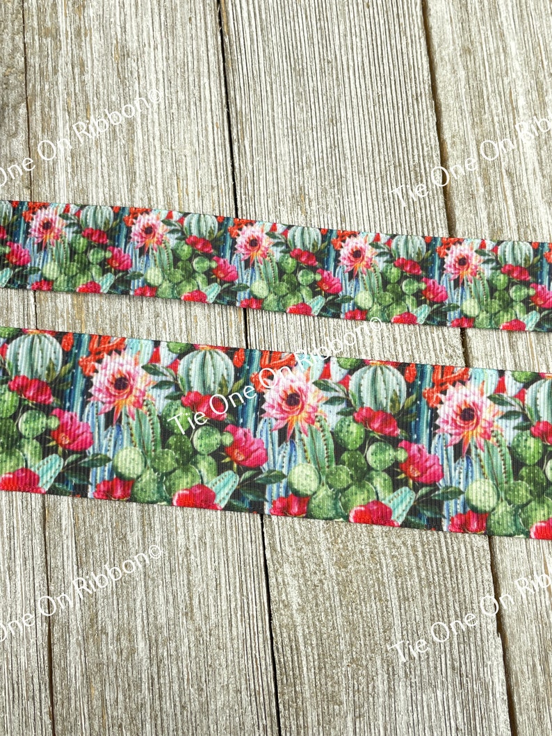 May include: A close-up of a colorful ribbon with a cactus and flower print. The ribbon is on a wooden surface.