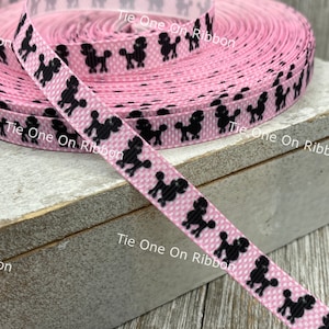 May include: Pink ribbon with a black poodle print. The ribbon is rolled up and the text "Tie One On Ribbon" is visible on the label.
