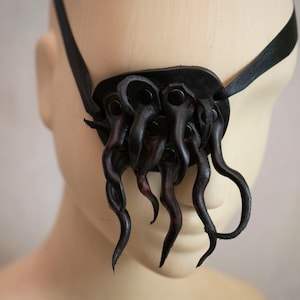 Può includere: Parche per l'occhio in pelle nera con un design a tentacoli. Il cerotto è attaccato a un cinturino nero.