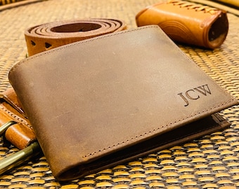 May include: A brown leather wallet with the initials "J.C.W." embossed on the front. The wallet is lying on a woven surface.