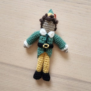 May include: A green and yellow crocheted elf doll with a brown yarn hair and a pointed hat.