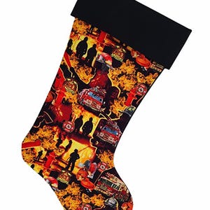 May include: Christmas stocking with a black cuff and a vibrant pattern featuring firefighters, fire trucks, and flames in shades of red, orange, and yellow. The stocking has a loop for hanging.