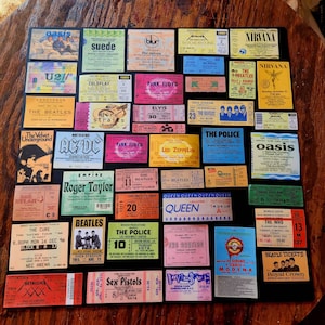 K&ouml;nnte beinhalten: Eine Sammlung von Vintage-Konzertkarten mit verschiedenen Bands, darunter Oasis, Nirvana, The Beatles, Queen und The Police. Die Tickets werden auf einer dunkelbraunen Holzoberfl&auml;che ausgestellt.