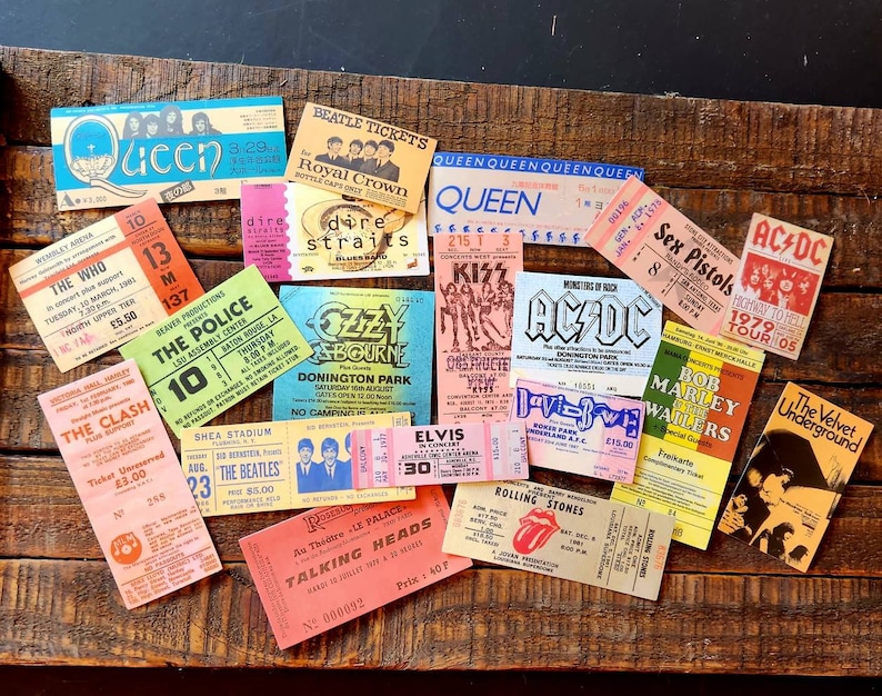K&ouml;nnte beinhalten: Eine Sammlung von Vintage-Konzertkarten mit Bands wie Queen, The Who, The Police, The Clash, The Beatles, Ozzy Osbourne, KISS, AC/DC, Sex Pistols, Bob Marley, The Velvet Underground, Talking Heads und Elvis Presley. Die Tickets sind auf einer Holzoberfl&auml;che angeordnet.