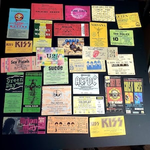 K&ouml;nnte beinhalten: Eine Sammlung von Vintage-Konzertkarten mit verschiedenen K&uuml;nstlern, darunter KISS, The Beatles, Green Day, U2 und Guns N' Roses. Die Tickets werden auf einer schwarzen Oberfl&auml;che angezeigt und weisen eine Vielzahl von Farben, Schriftarten und Designs auf.