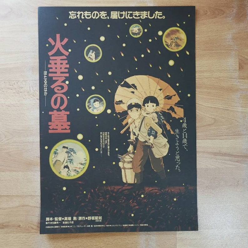 May include: A vintage Japanese movie poster for the film "Grave of the Fireflies" (火垂るの墓) with a black background and a scene of two children walking in the rain with an umbrella. The poster features the Japanese text "忘れものを、届けにきました。" (I came to deliver something I forgot) and "火垂るの墓" (Grave of the Fireflies).