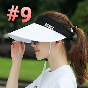 May include: White sun visor with a black band and a black strap. The band has the text "KDA.KBT" printed on it.