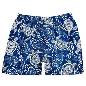 May include: Blue shorts with an all-over pattern of white sea turtles, waves, and fish. The shorts have an elastic waistband. The fabric has a textured appearance.