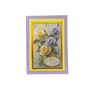 May include: A handmade greeting card with a lavender border and a yellow inner frame. The card features yellow and lavender roses with green leaves. An oval emblem at the bottom displays the number "100".