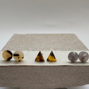 May include: Three pairs of earrings, one pair is round and brown with white swirls, one pair is triangular and brown with yellow swirls, and one pair is round and gray with white swirls.