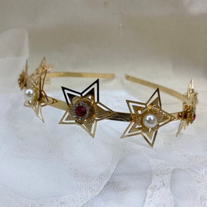 May include: Gold headband with five star-shaped cutouts, each decorated with a pearl or red rhinestone.