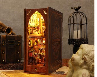 Pode incluir: Uma caixa de madeira em forma de livro com uma cena de biblioteca em miniatura dentro. A caixa é decorada com detalhes intrincados e tem um título que diz "Library of Dreams".