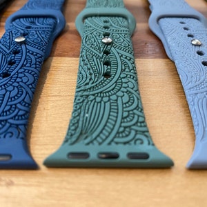 May include: A collection of silicone watch bands featuring intricate embossed paisley patterns. The bands are available in various colors including dark blue, sage green, light blue, and black, each with a metallic pin closure and multiple adjustment holes.