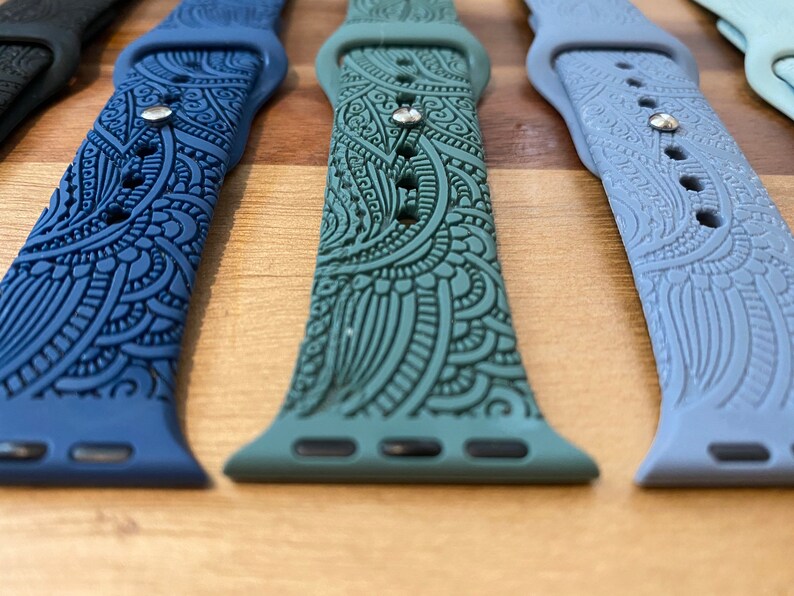 May include: A collection of silicone watch bands featuring intricate embossed paisley patterns. The bands are available in various colors including dark blue, sage green, light blue, and black, each with a metallic pin closure and multiple adjustment holes.