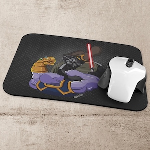 Puede incluir: Una alfombrilla de ratón negra con un fondo gris oscuro que presenta una imagen de dibujos animados de Darth Vader y Thanos luchando en un pulso. El texto "dub.this" está impreso en blanco en la alfombrilla del ratón.
