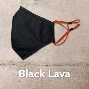 Peut inclure: Masque facial noir avec des boucles d'oreille r&eacute;glables orange. Le masque est fait d'un tissu doux et respirant. "Black Lava" est &eacute;crit en blanc sous le masque.