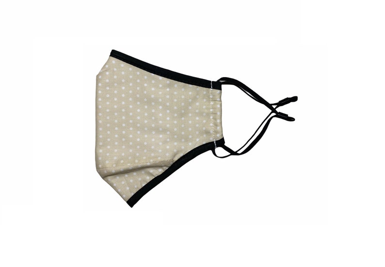 May include: A beige face mask with white polka dots and black elastic straps.