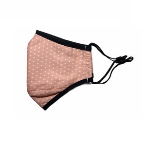 May include: A pink face mask with white polka dots and black elastic ear loops.