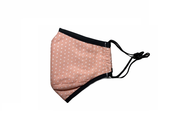 May include: A pink face mask with white polka dots and black elastic ear loops.